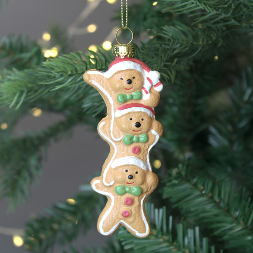A view of three stacked gingerbread figurines wearing Santa hats, holding hands, adorned with colourful decorations hanging on a Christmas tree