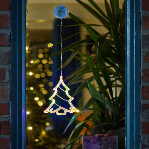 A glowing Christmas tree decoration hangs in a window, with a blurred background of festive lights and greenery.