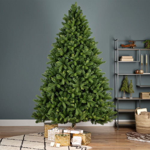 Large artificial Christmas tree with dense green foliage displayed in a contemporary living room, creating a striking festive centrepiece alongside wrapped Christmas gifts.