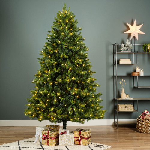 Pre-lit artificial Christmas tree displayed indoors with wrapped presents, featuring warm white LED lights, dense green foliage and a full traditional shape for festive home décor.