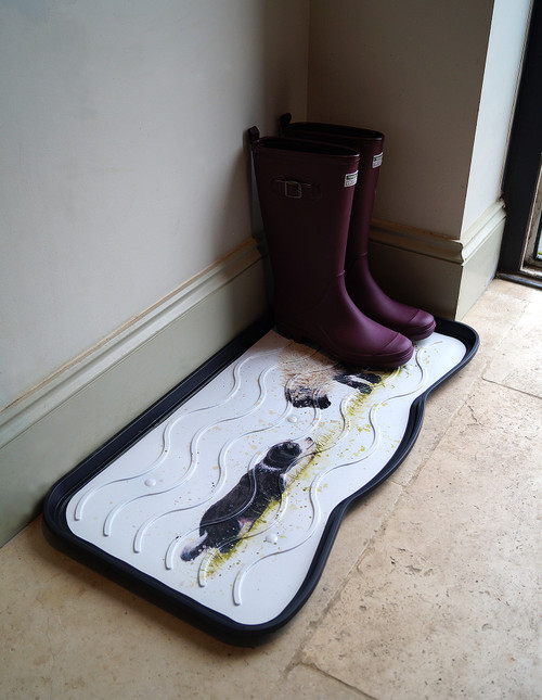 A tray in a hallway that has a pair of wellingtons stored on it, it has a sheep and and a dog meeting each other printed on it.