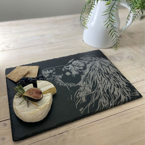 A slate cheeseboard with a laser engraved spaniel image, laid upon a table with a selection of cheeses.