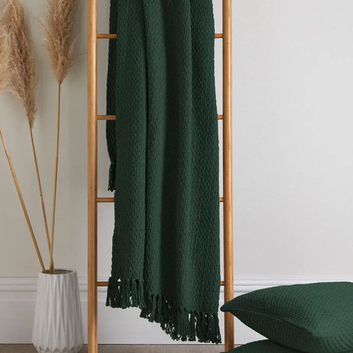 A dark green weave throw hanging off a ladder next to a pampas grass.