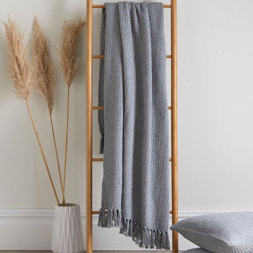 A grey weave throw hanging off a ladder next to a pampas grass