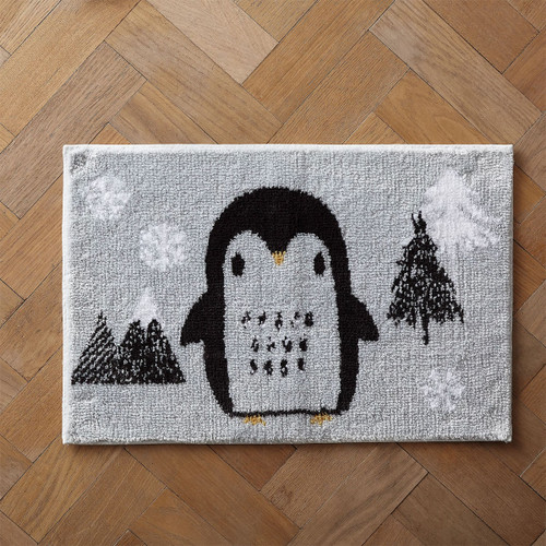 A cute penguin-themed bath mat on a herringbone wood floor.