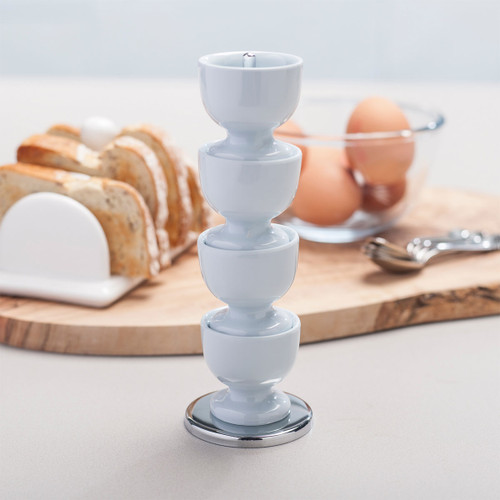 A stack of light blue egg cups on a table, with sliced bread and eggs in the background.