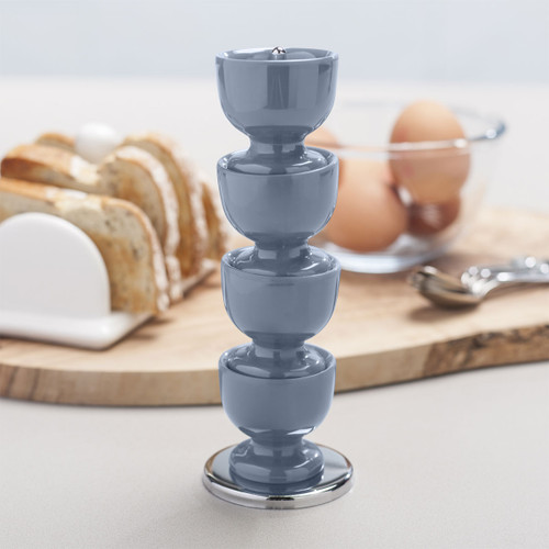 Stacked blue egg cups on a counter with sliced bread and eggs in the background.