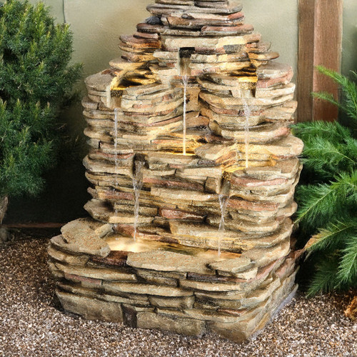 A tiered stone garden fountain with cascading water surrounded by green plants, creating a serene and natural outdoor ambiance.