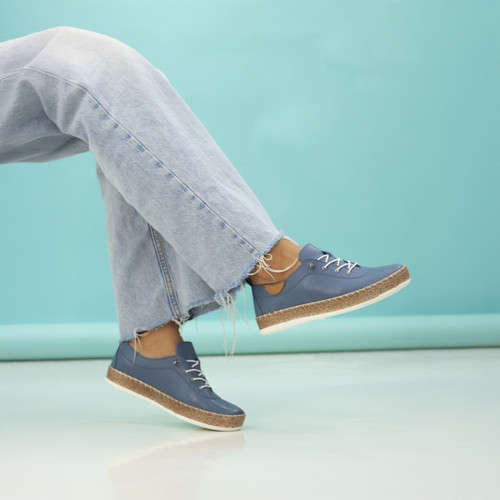 A person wearing blue shoes and frayed jeans with crossed ankles, suspended in air against a teal background.
