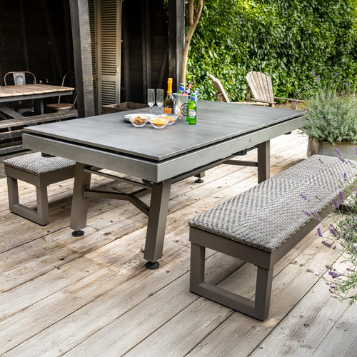 A modern outdoor dining table set with drinks and snacks, surrounded by lush greenery and wooden flooring.