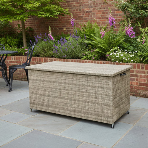 Large rattan garden storage box with lid on a patio, set against a brick wall and flower garden.
