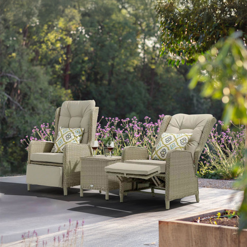 Cosy outdoor seating with two beige recliners, decorated with patterned cushions, beside a small table and surrounded by purple flowers.