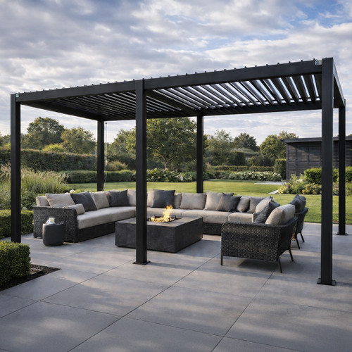 Modern outdoor pergola with a black metal frame and slatted roof covering a patio seating area with cushioned wicker sofas and chairs arranged around a square fire pit table, set in a landscaped garden with lawn, shrubs, and trees under a cloudy sky.