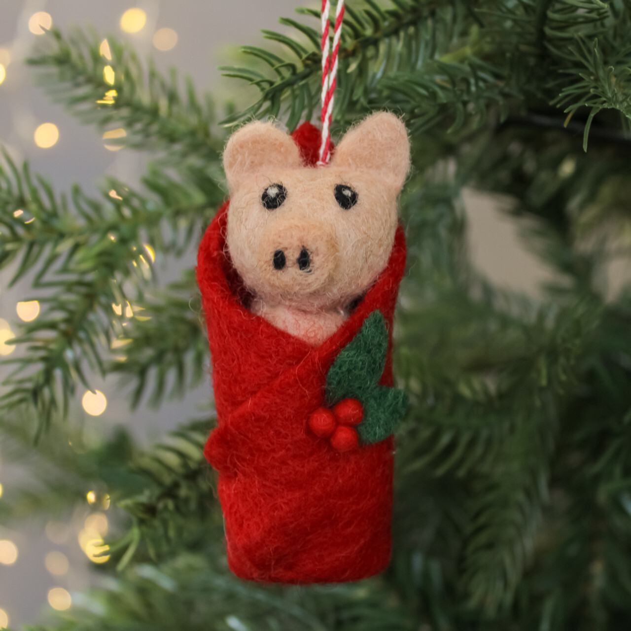 A felt Christmas decoration shaped like a pig in a red blanket.