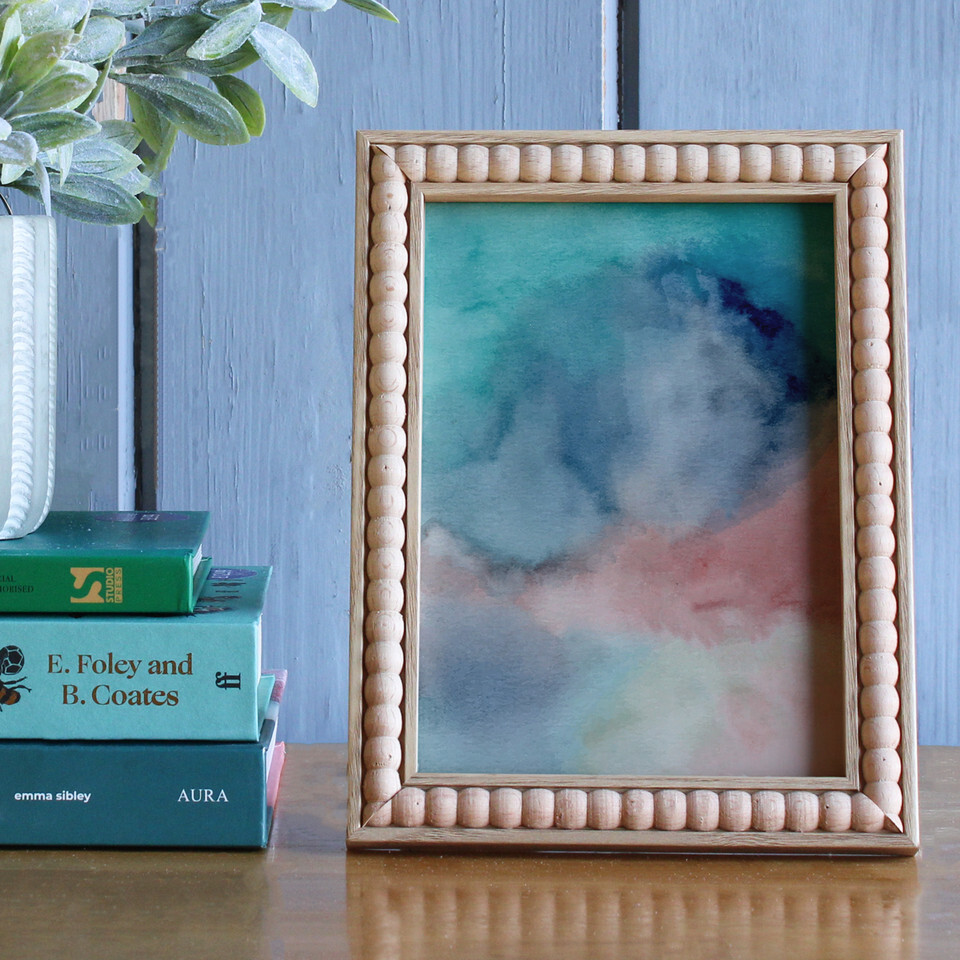 A view of a bobbled wooden photo frame on a wooden table in front of a wooden blue background next to some books. 