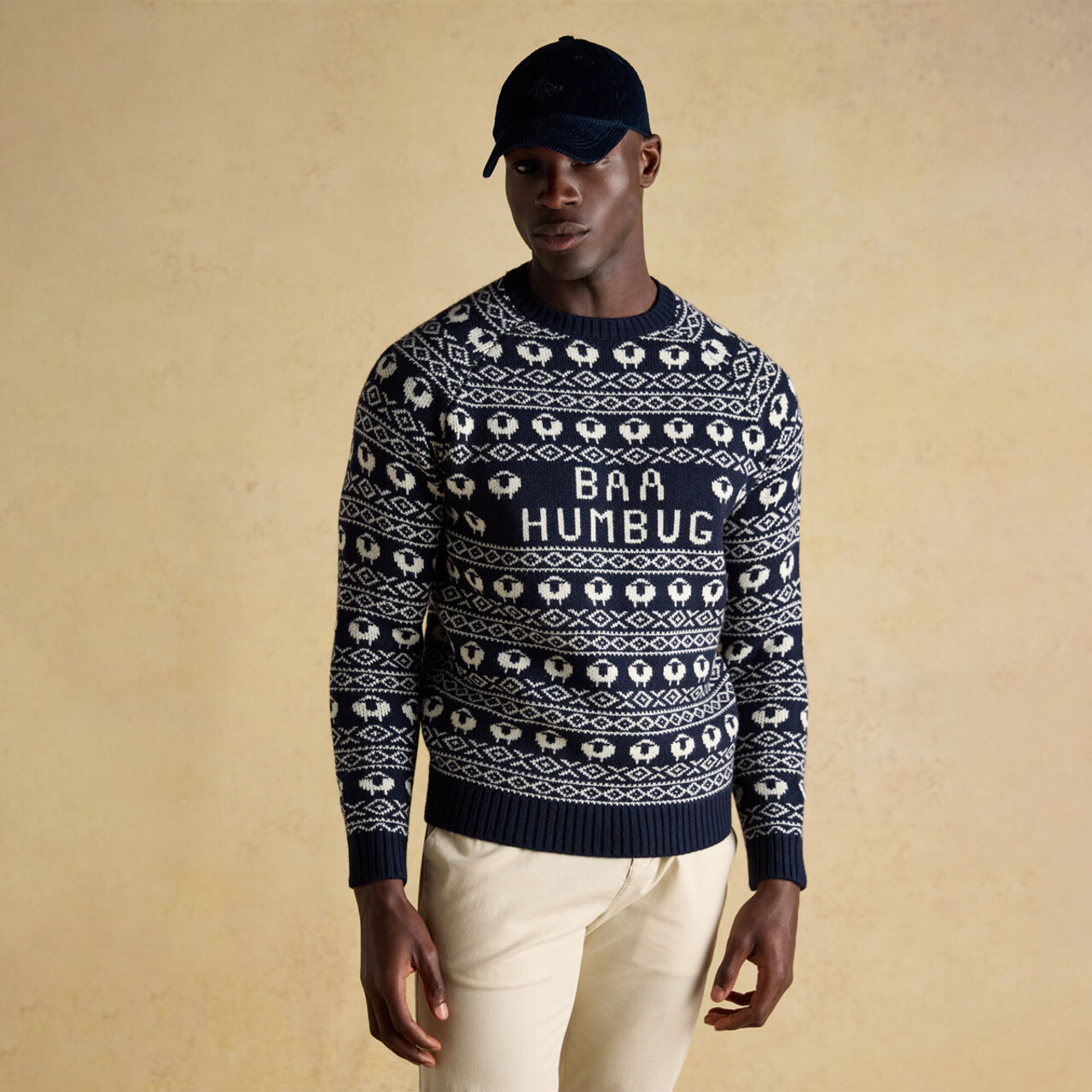 A man wearing a navy Joules jumper with a festive sheep print and 'Baa Humbug' written in the centre.
