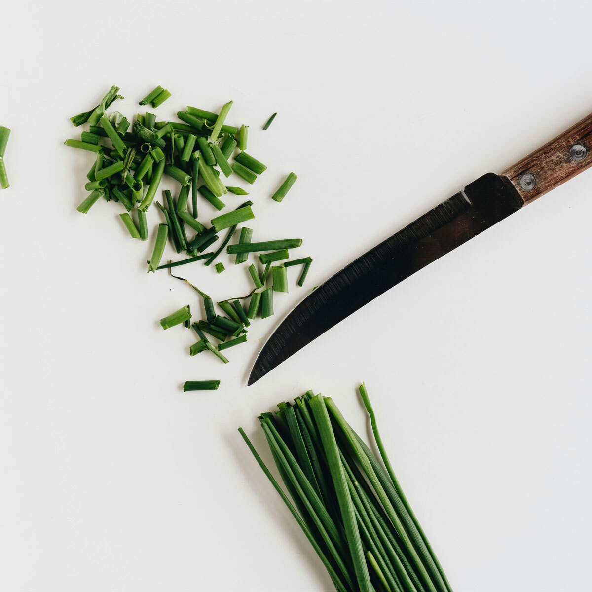 A view of a knife cutting up herbs on a white background