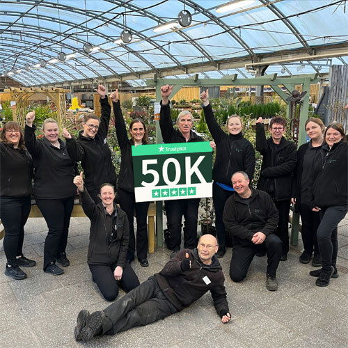 Charlies staff stood in a garden centre holding a sign stating 50,000 trustpilot reviews