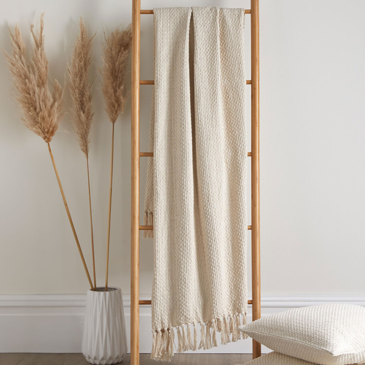 A cream coloured woven throw blanket draped over a wooden blanket ladder.