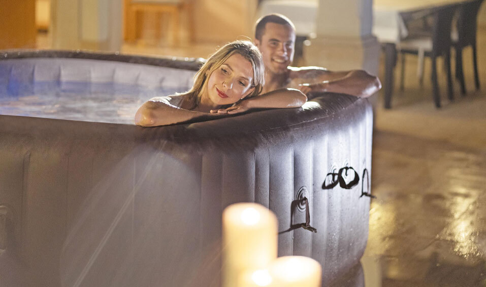 Couple unwinding in an inflatable hot tub at night, resting arms on the edge with warm lighting and a calm, relaxing atmosphere.