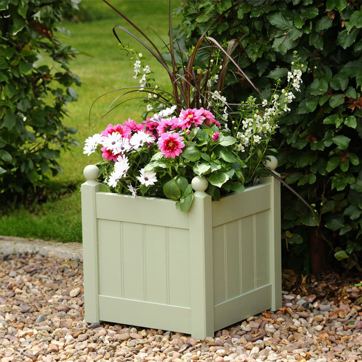 A view of a wooden blanter filled with pink and white flowers in a garden
