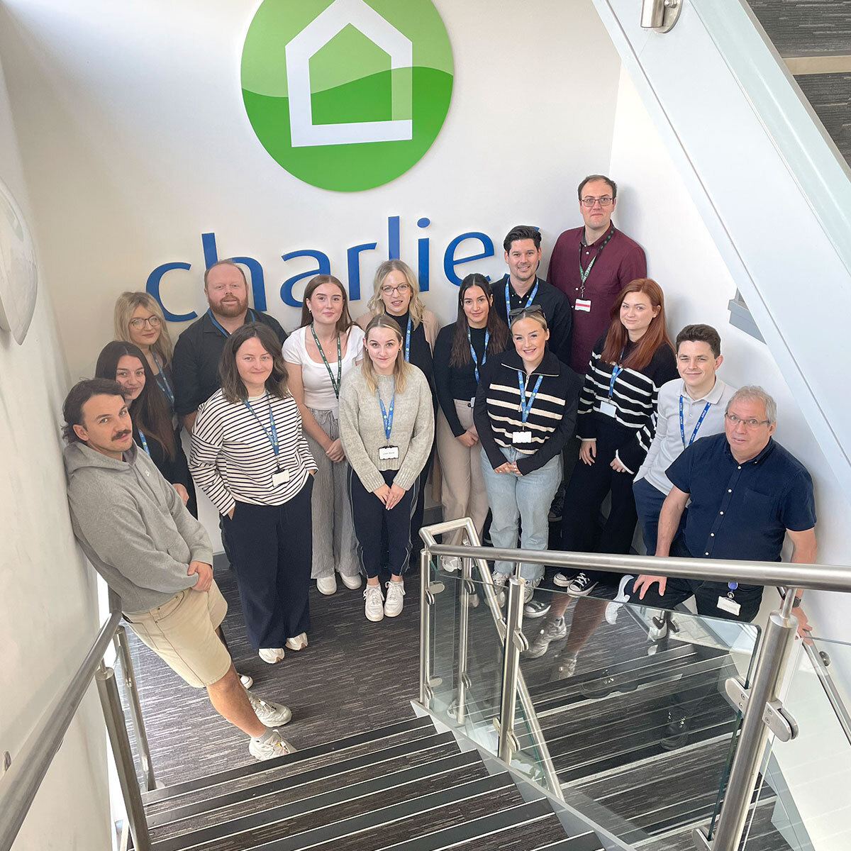 Charlies staff stood on the stairs in an office in front of a large Charlies logo