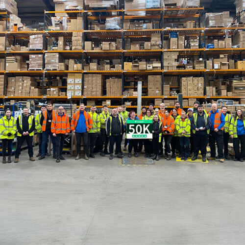 Charlies staff stood in a large wearhouse holding a sign stating 50,000 trustpilot reviews