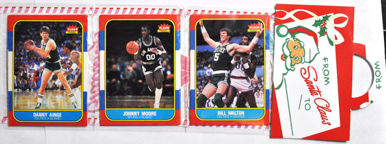 Image 1 (Danny Ainge, Johnny Moore, Bill Walton + Santa Tag): “Vintage 1986 Fleer Basketball trading cards featuring Danny Ainge, Johnny Moore, and Bill Walton with festive Santa Claus gift tag. Holiday-themed collectible pack highlighting iconic Fleer Premier design, perfect for basketball card collectors chasing the Michael Jordan rookie card.”