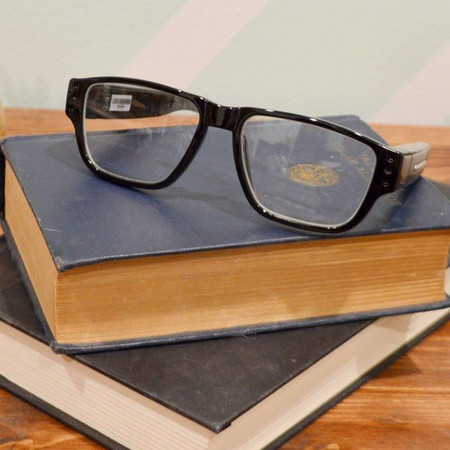 Lawmate Professional Grade Covert Surveillance Glasses, black stylish glasses with hidden recording device, on top of stacked books.