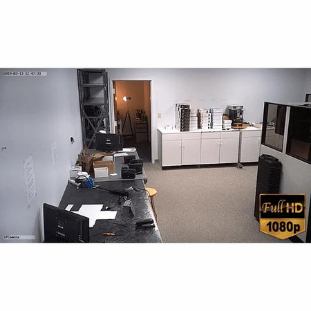 4G LTE All-in-One Battery Powered Wall Clock Security Camera, video only, capturing an office room with desks, computers, office supplies, and a large monitor, showing a security surveillance view in Full HD 1080p resolution.