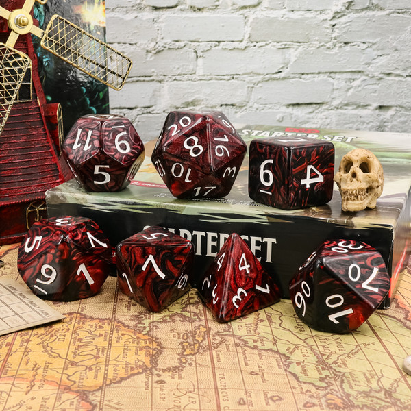 Picture shows a full set of 7 deep pearl red and black swirled acrylic jumbo dice with white numbers arranged horizontally with 3 of them on top of a box and 4 in front of the box. Set includes 55mm d20 with proportionally scaled d12, d10, d%, d8, d6, and d4.