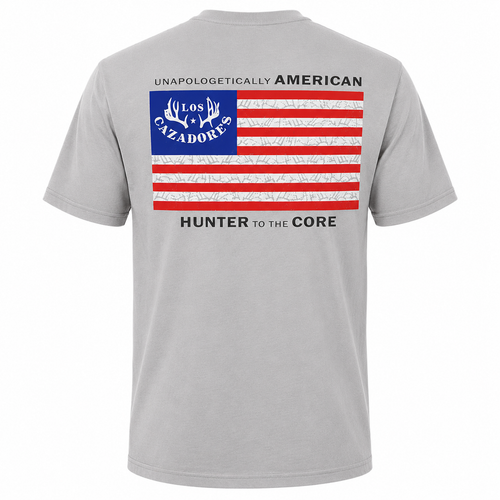 Back view of a Los Cazadores adult short-sleeve t-shirt displayed on an invisible ghost mannequin against a white background. The light gray crew neck tee features a large patriotic American flag graphic centered on the upper back with a blue canton containing the Los Cazadores antler logo, distressed red and white stripes, and the phrase “Unapologetically American” above the flag. Below the graphic, the shirt displays the text “Hunter to the Core.” Clean ecommerce-style product image showcasing the full back design and classic fit.