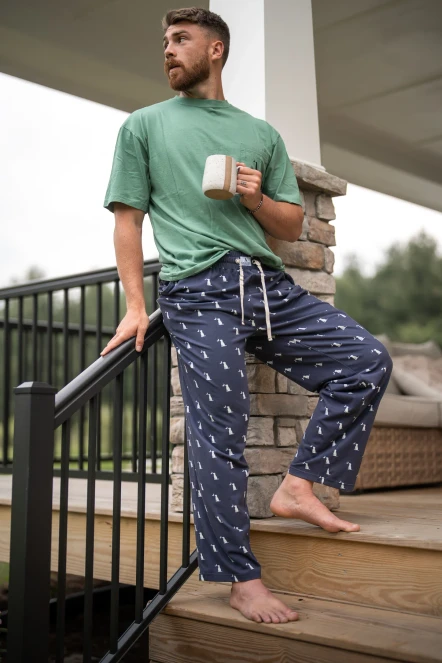 Man sitting on porch steps with a mug wearing Local Boy pajama pants in navy dog and moon