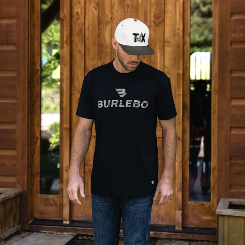 Man in a cap wearing the Burlebo black Flying B logo tee in front of a wooden door