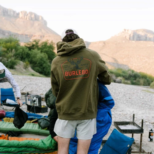 Man wearing the Burlebo big game hunts fleece hoodie at a desert river campsite, back view
