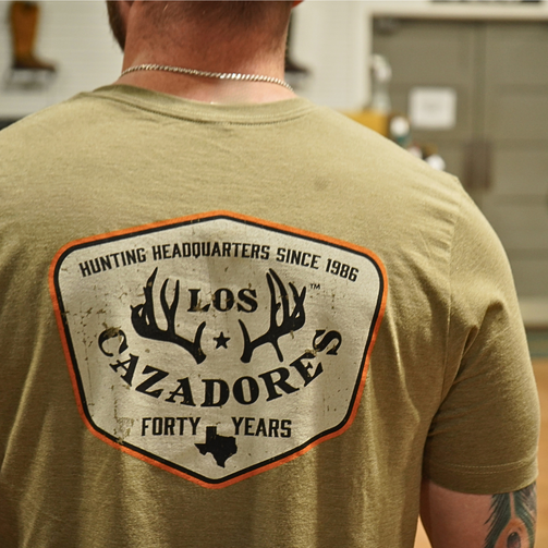 close up view of the back side of an individual wearing the los cazadores special edition 40th year badge short sleeve tee.