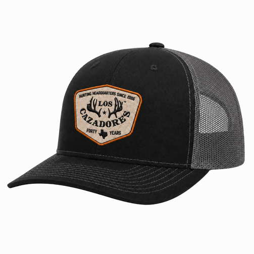 Whitebox image of Los Cazadores trucker cap featuring a black front panel, curved brim, gray mesh back, and commemorative “Forty Years” front patch.