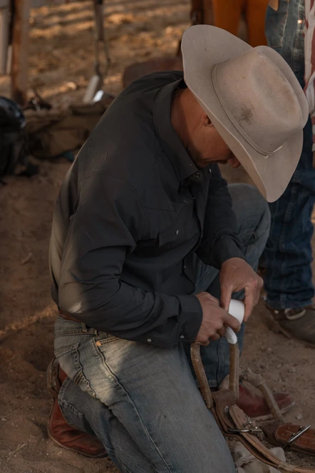 Cowboy kneeling to work on tack at a rodeo arena in the Ferrell CORE long sleeve pearl snap shirt in Grey