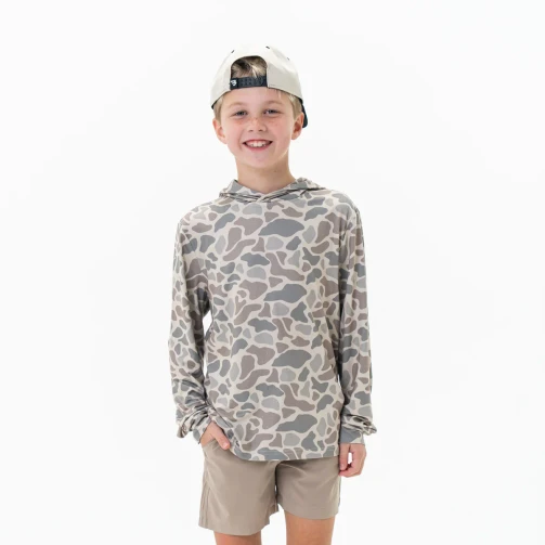 Kid wearing the Burlebo youth performance hoodie in a light grey and tan camo, with a cap