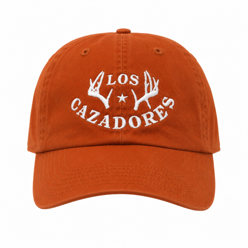 Front view of the Los Cazadores rust orange cap with white horn logo embroidery on a clean white background.