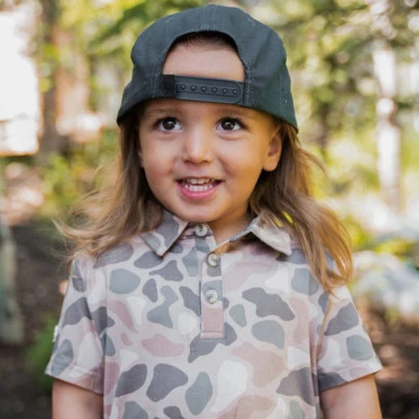 Young girl wearing the Burlebo youth performance polo in pintail camo outdoors