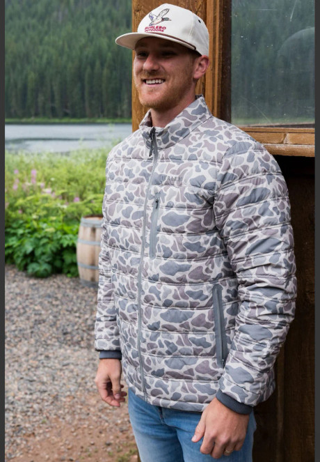 Man wearing the Burlebo puffer jacket in classic deer camo by a lake