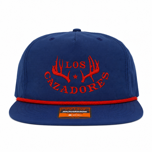 Front vieFront view of a royal blue Los Cazadores rope hat with red embroidered logo and red rope detail on white.