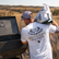 back side of a male model wearing the los cazadores 40 years short sleeve tee while filling a protein feeder in a pasture.