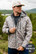 Man outdoors wearing the Burlebo challenger jacket in classic deer camo with an also available in 3XL badge