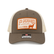 Front view of a Los Cazadores trucker hat with taupe front panels, cream mesh back, orange patch, and curved brim on a white background.