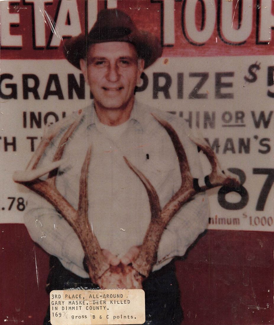 Gary Maske in a cowboy hat holds a set of antlers in front of the red Grand Prize tournament sign