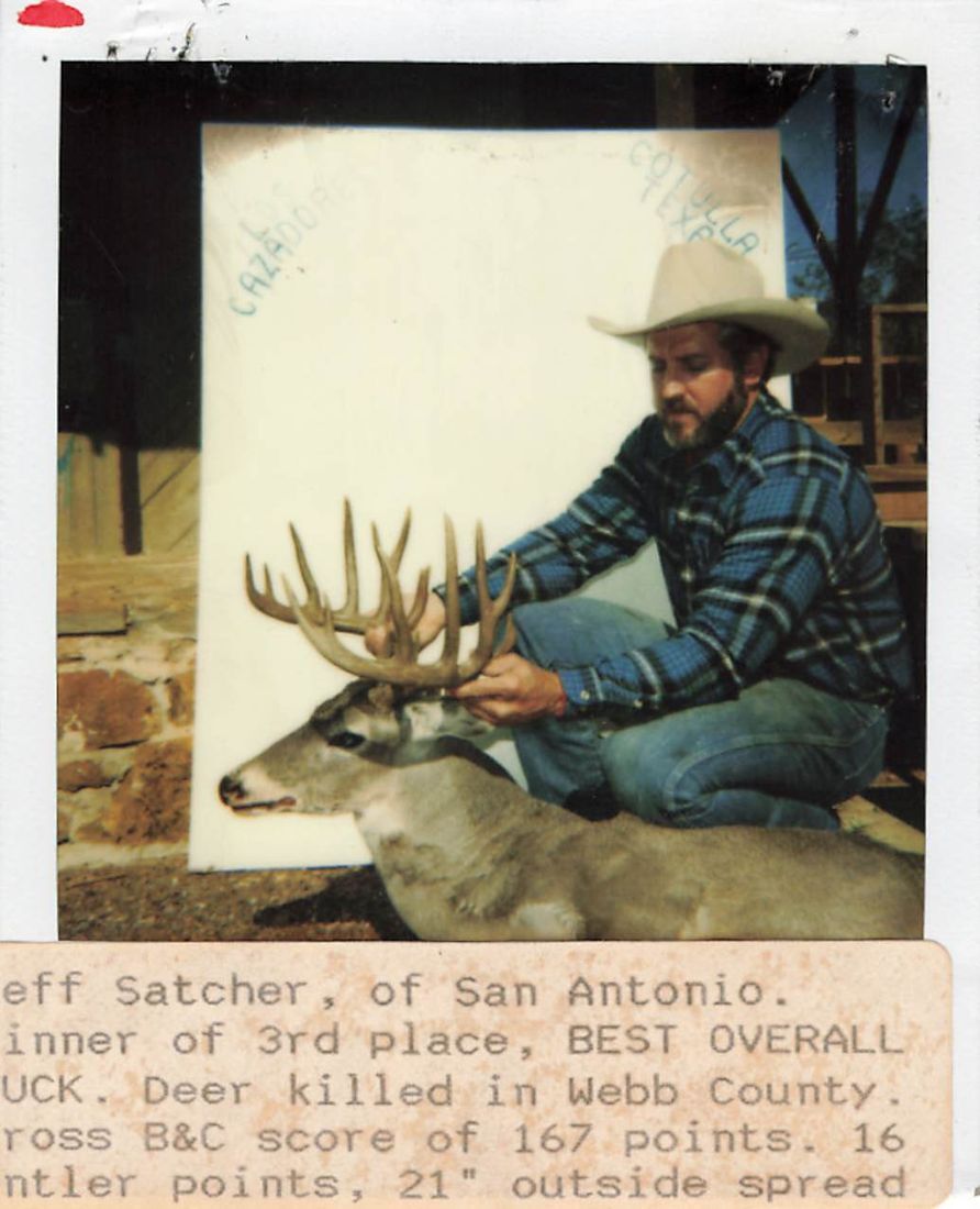 Jeff Satcher in a cowboy hat kneels beside his buck in front of a Los Cazadores Cotulla, Texas backdrop