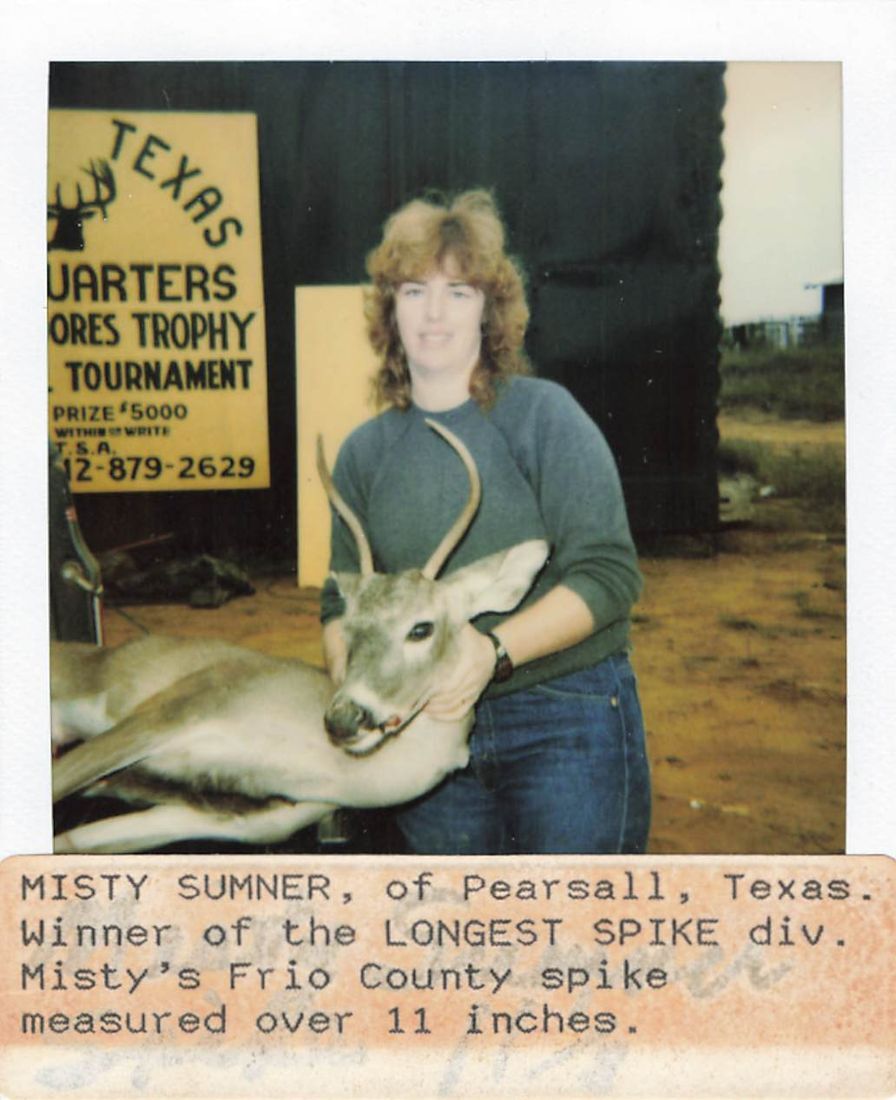 Misty Sumner kneels beside her spike buck in front of the South Texas Headquarters tournament sign