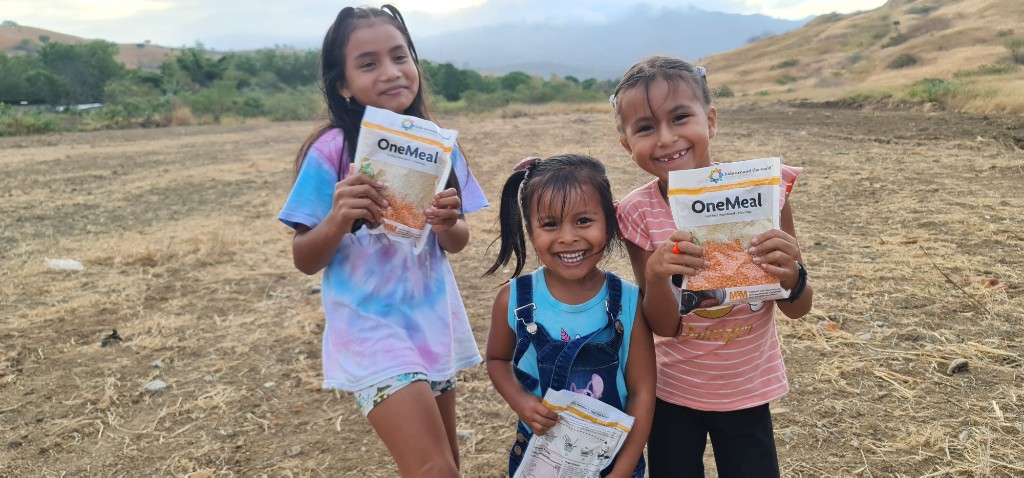 Children holding OneMeal nutritional packets in a Hope Zone community